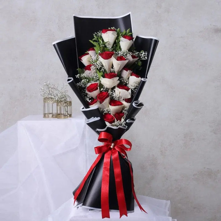 A hand bouquet of red and white roses with elegant black and red packaging.