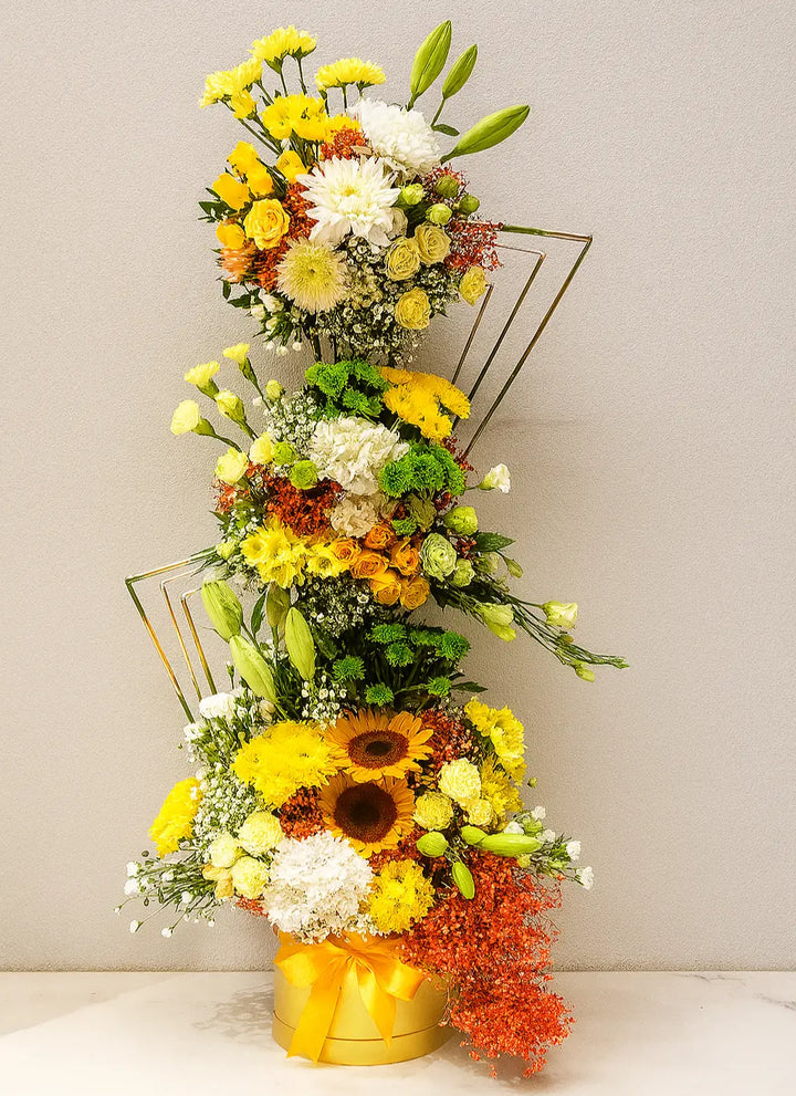 Tall floral arrangement with sunflowers, yellow, orange, and white flowers on a gray background