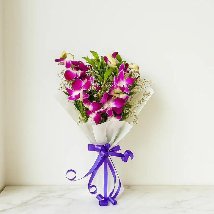 Bouquet of purple orchids with a purple ribbon on a white marble surface.