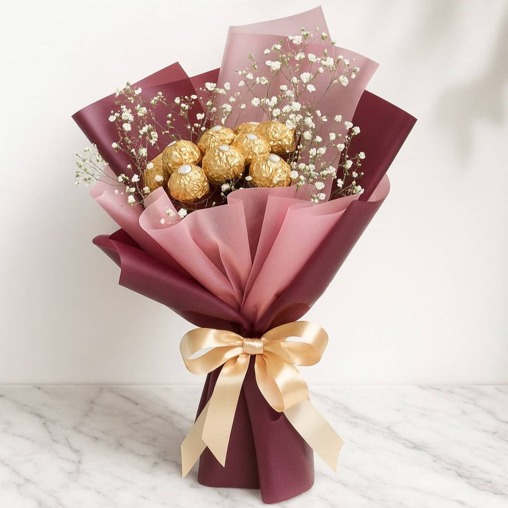 Bouquet of flowers wrapped in pink paper with gold ribbon and Ferrero Rocher chocolates on a marble surface. Chocolate Bouquet