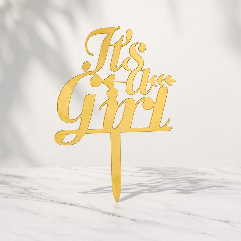 Gold 'It's a Girl' cake topper on a marble background